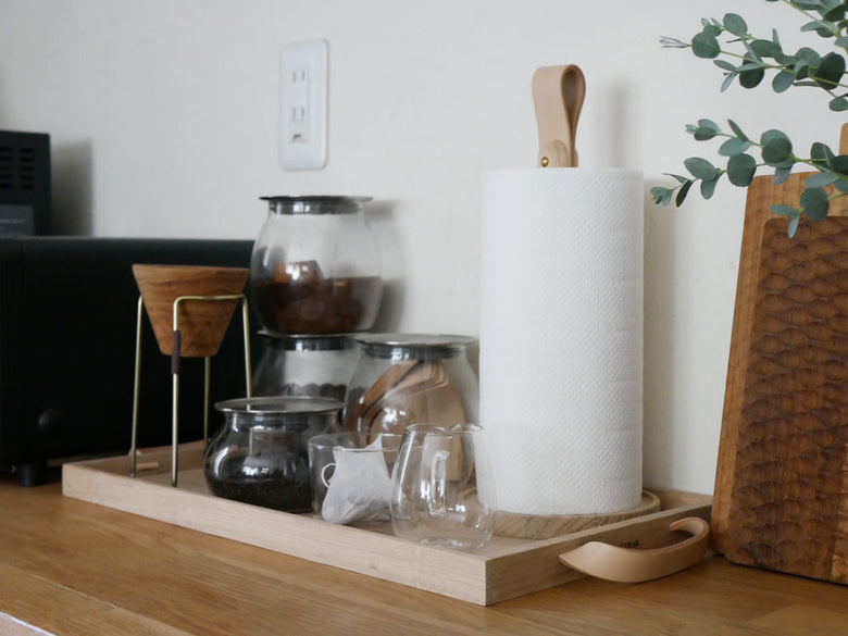 フリッツ・ハンセンのSkagerak Norrトレイ上に、オークとレザー製のテーブルウェア、カップ、キッチン用品、カッティングボードが配置されている様子