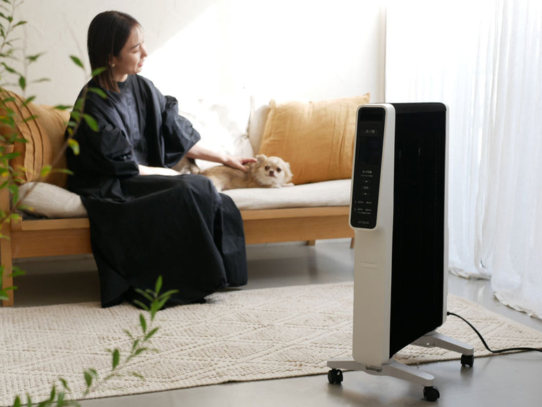 リビングルームの木製フロアに置かれたシロカ製遠赤軽量ヒーター「かるポカ」。周囲に家具が配置され、快適な空間を提供する様子。