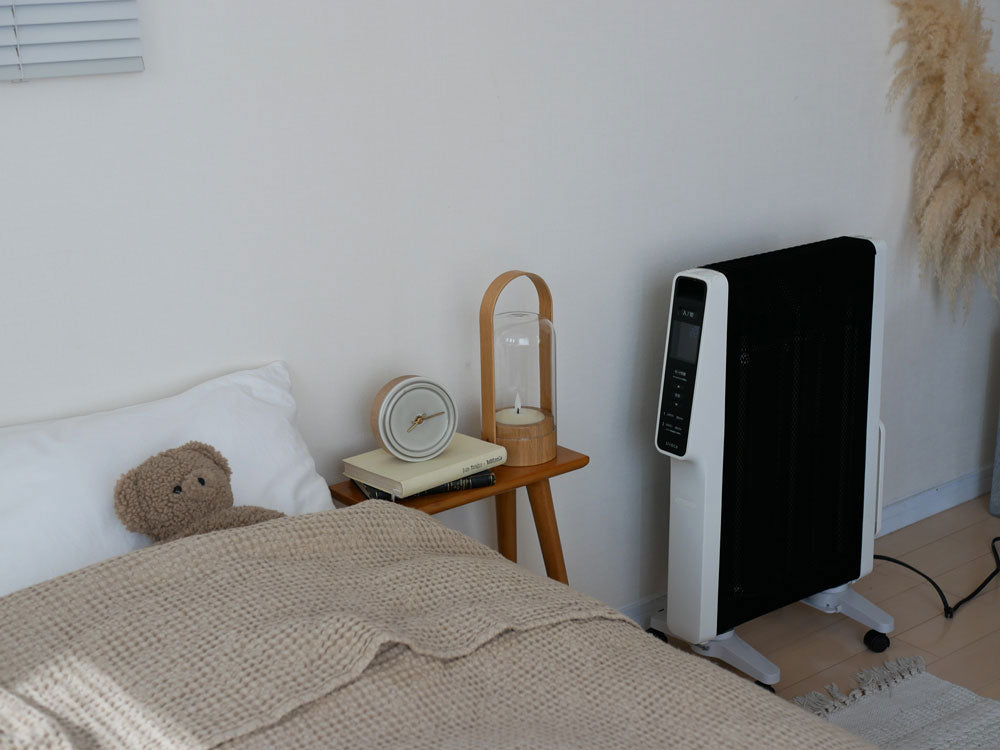 リビングルームに設置されたシロカの遠赤外線軽量ヒーター「かるポカ」と木製家具、観葉植物、ランプが調和した家庭用電化製品の画像