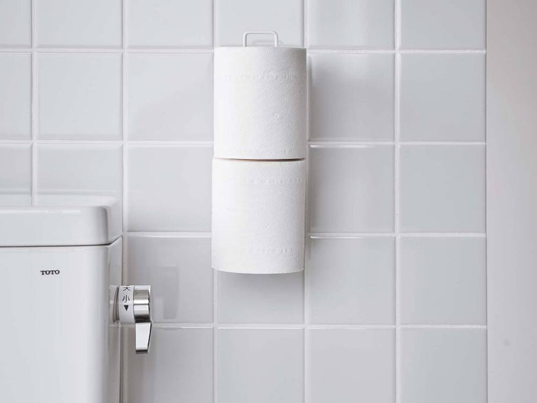 白色のスチール製トイレットペーパーホルダーが壁に取り付けられ、トイレットペーパーがセットされている様子