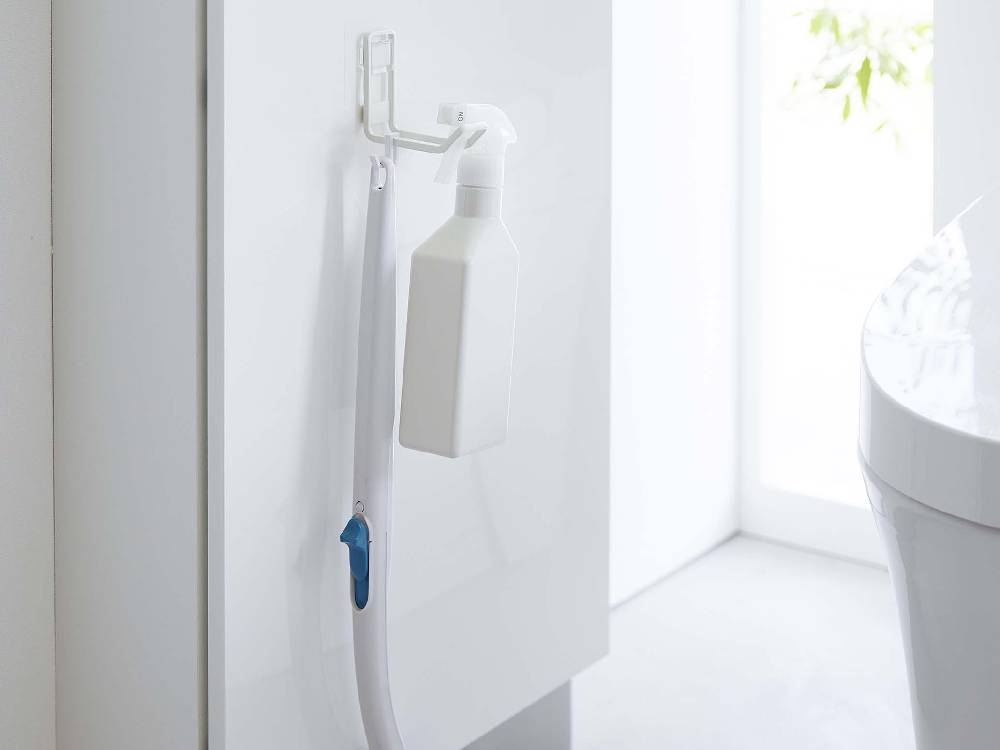 タワーのフィルムフックトイレ用品収納フックがバスルームのタイル面に取り付けられ、プラスチック製のソープディスペンサーやその他の洗面用具が掛けられている様子