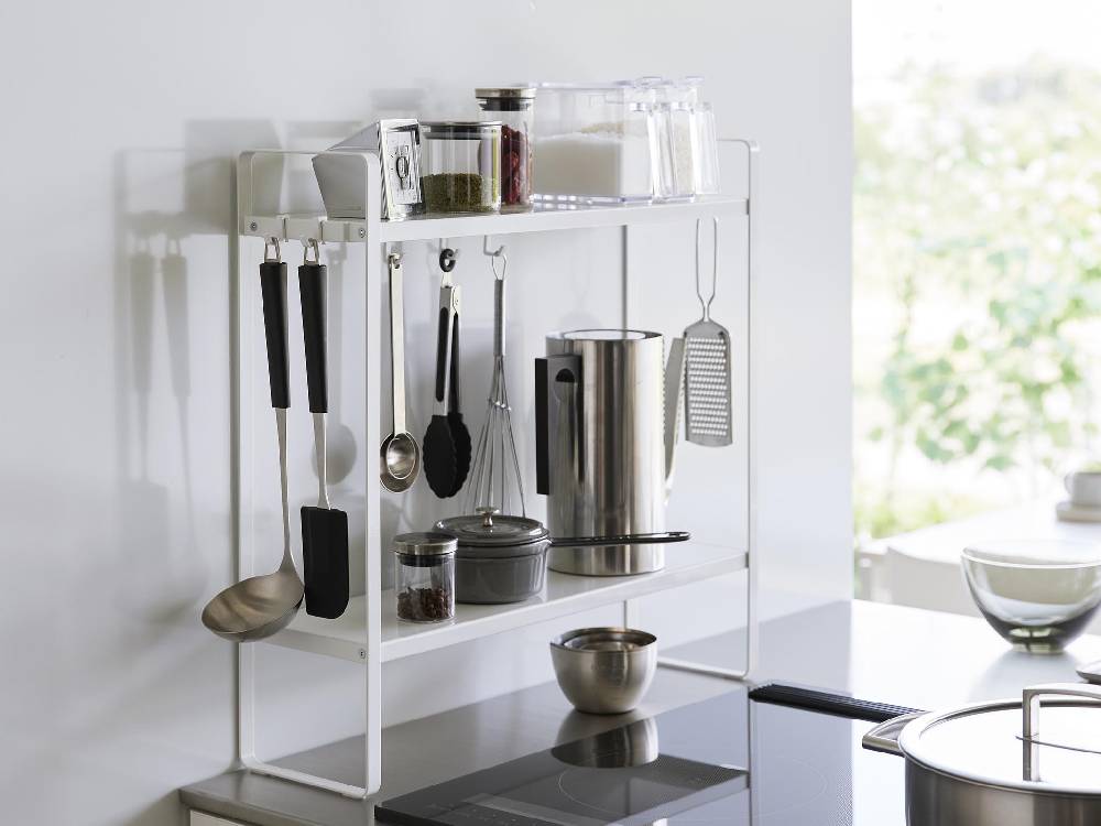 タワー下が拭けるコンロ横ラック2段がキッチンカウンターに設置され、スチール製の上段と下段に調理器具や小型家電が整理されています