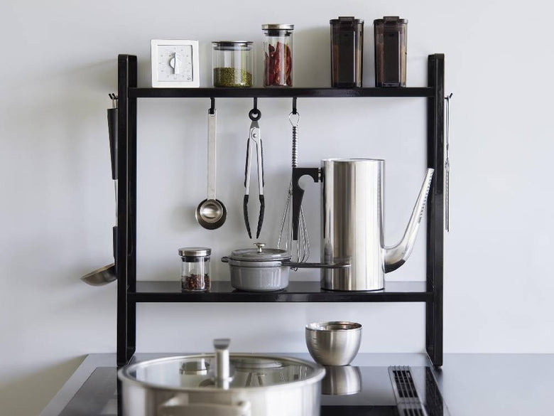 キッチンのコンロ横に設置されたスチール製の2段シェルフ「tower」で、上段と下段に調理器具や鍋が整然と収納されている様子