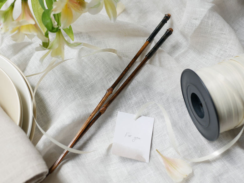 公長斎小菅の黒竹と籐製のおもてなし用取り箸1膳。26cmの高級箸は拭き漆塗装が施され、自然素材の美しい模様が特徴です。