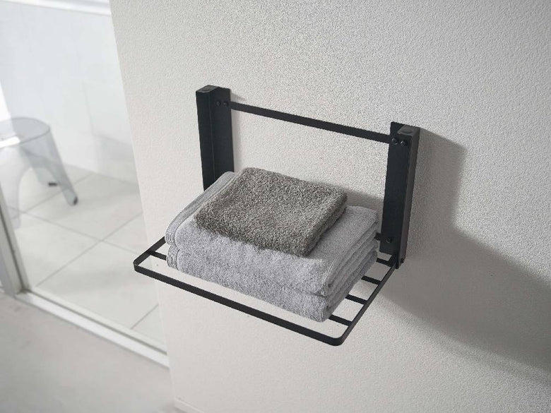 タワー折りたたみ棚がバスルームの石こうボード壁に設置されており、バスケットやトイレットロールホルダーが収納されている様子