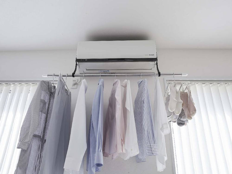クローゼット内の天井に取り付けられた銀色のパイプとニッケル仕上げのフックを備えた室内物干しポールホルダーに、衣類ハンガーやカーテンが掛けられている様子