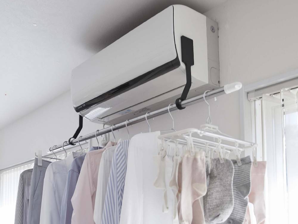 タワーのフィルムフックエアコン室内物干しポールホルダーがエアコン横に設置され、服をハンガーに掛けている様子