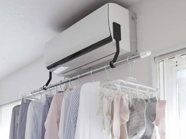 タワーのフィルムフックエアコン室内物干しポールホルダーがエアコン横に設置され、服をハンガーに掛けている様子