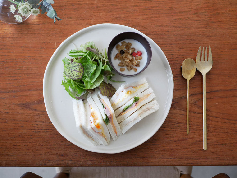 食洗機対応の天然木カップとテーブルウェアがサンドイッチや野菜と共にテーブルに配置されている様子