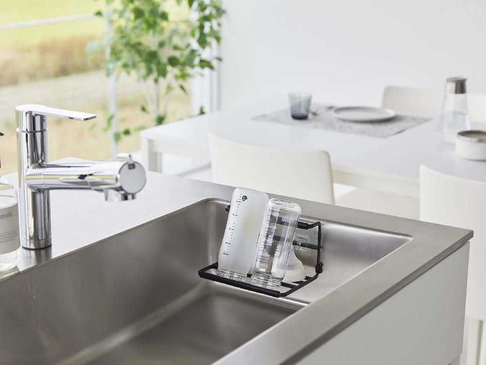 タワー製フィルムフックワイドジャグボトルホルダー Sがキッチンシンクに取り付けられ、ジャグボトルやマグカップを整理している様子