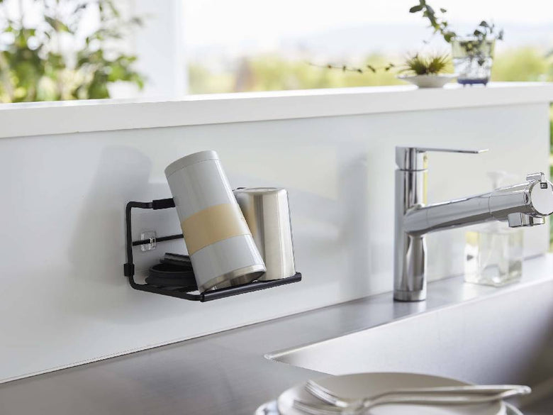 キッチンのシンク横に取り付けられたスチール製タワー型ボトルホルダー。ユニクロメッキ仕上げで、200mLから2Lのボトルを安定して収納。フィルムフックでタイル壁に固定されており、周囲には家庭用設備や植物が配置されている様子。