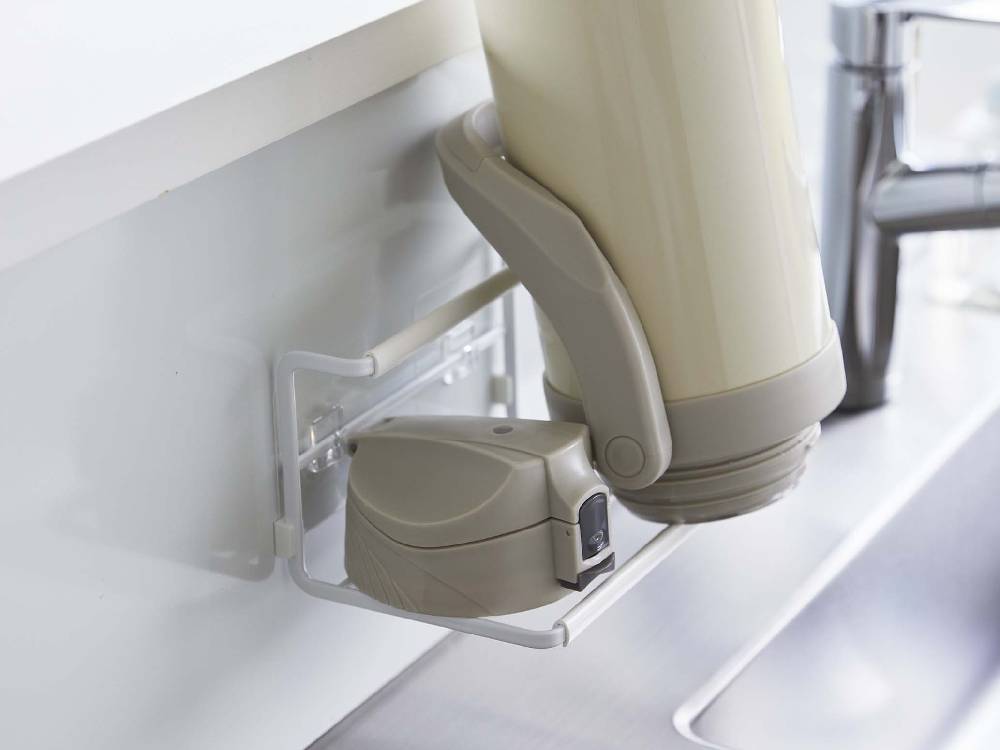 タワー製フィルムフックワイドジャグボトルホルダーSがキッチンのタイル壁に設置され、水筒やジャグボトルを整理している様子