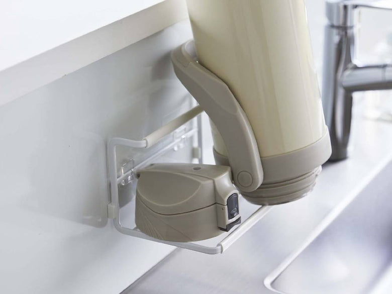 タワー製フィルムフックワイドジャグボトルホルダーSがキッチンのタイル壁に設置され、水筒やジャグボトルを整理している様子