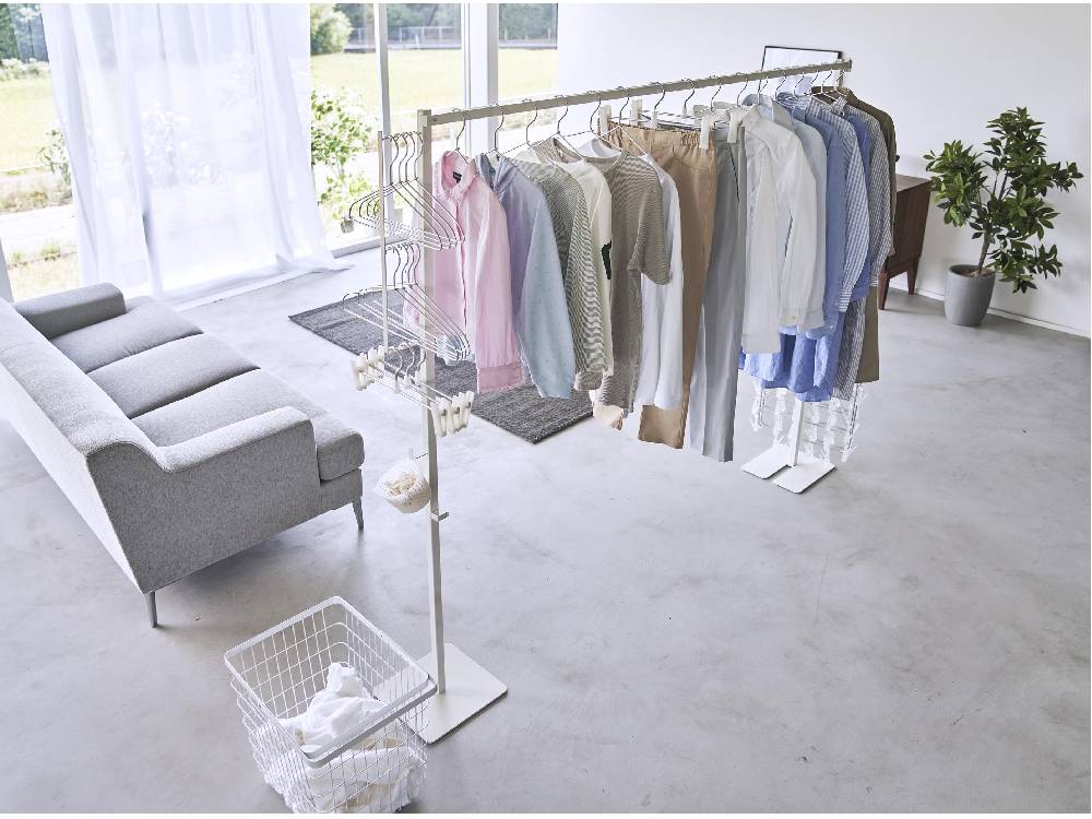 シルバー色の折り畳み式室内物干しタワーが自然素材風の床に設置され、アルミ製のハンガーが複数掛かっているデザイン