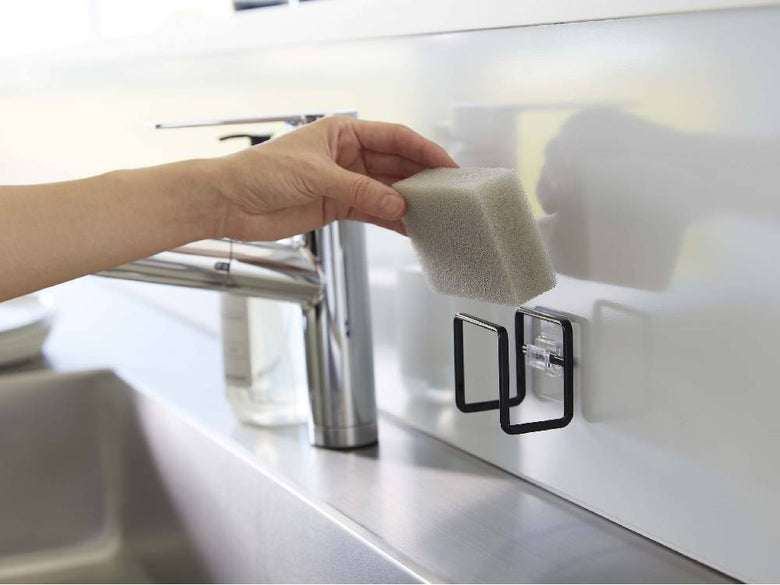 キッチンシンクに取り付けられたタワーシリーズのフィルムフックスポンジホルダー。スチール製でポリカーボネートのフィルムフックが備わり、耐荷重500gの耐久性を持つ