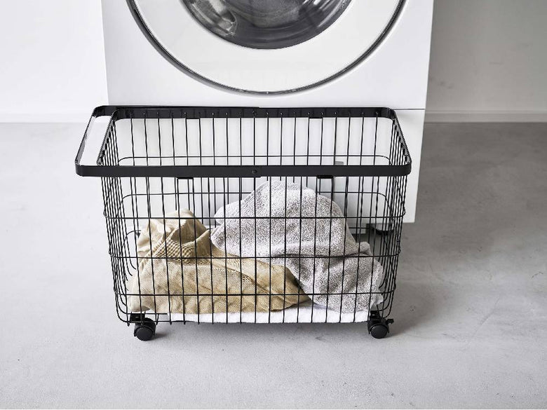 キャスター付きスチール製の灰色ランドリーバスケットが洗濯室で洗濯機やショッピングカートと共に配置されています。