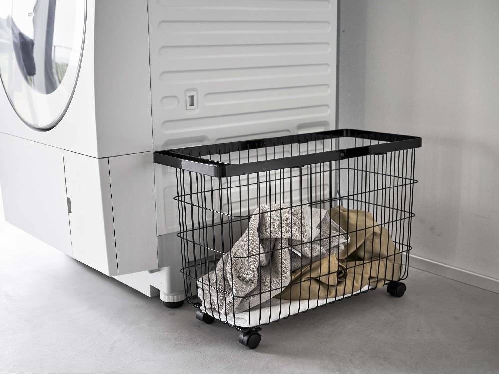 キャスター付きワイド&ローランドリーバスケットがグレーとシルバーの洗濯機・乾燥機の隣に配置された洗濯室の内部。