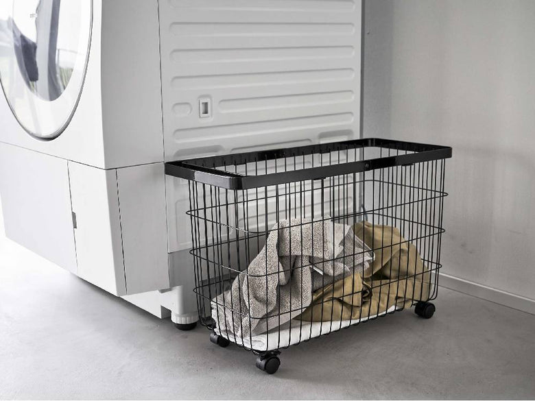 キャスター付きワイド&ローランドリーバスケットがグレーとシルバーの洗濯機・乾燥機の隣に配置された洗濯室の内部。