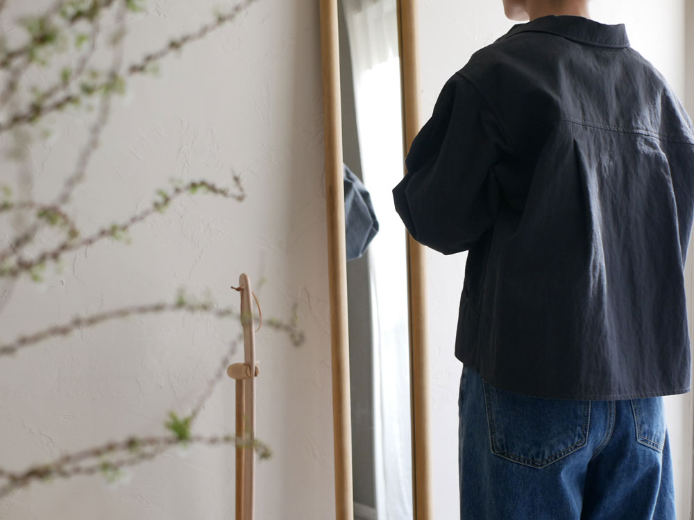 サンフラワーラタン製のHOKOS全身映るチークスリムミラーに、デニムの袖や襟、ポケットを持つ人の背中が映っています。