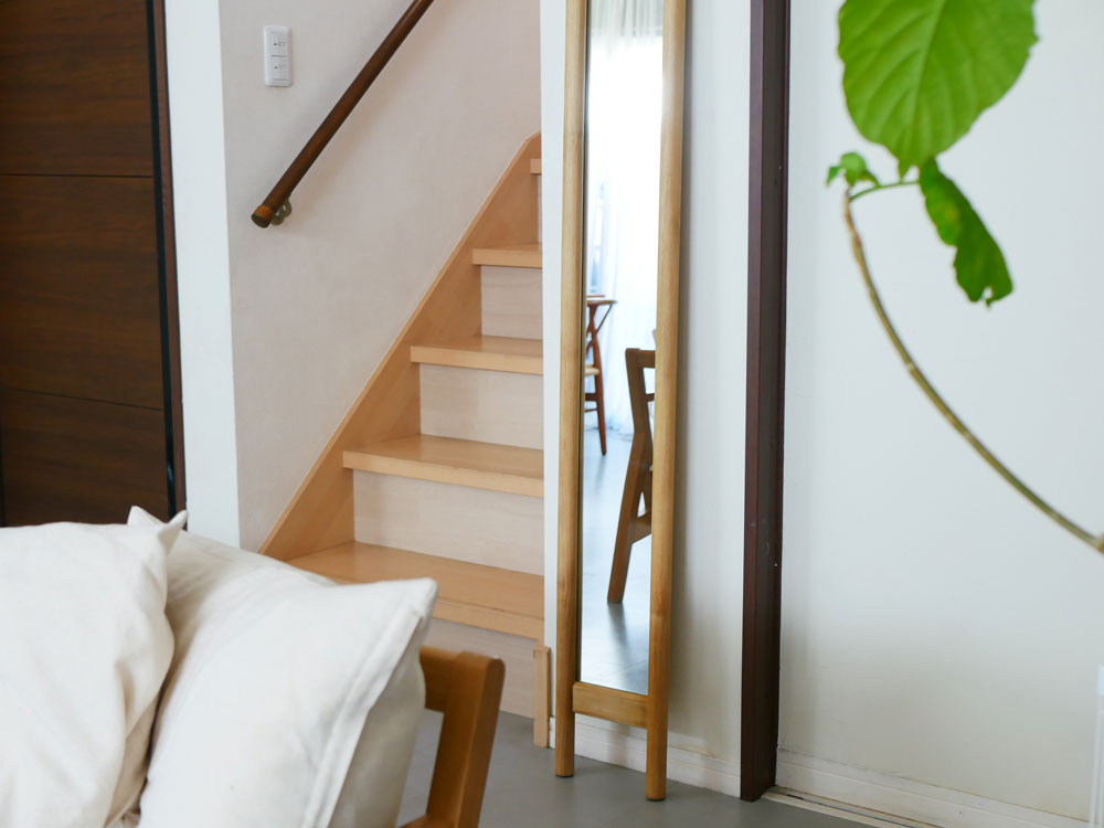 チーク無垢材とサンフラワーラタンを使用したHOKOS全身映るスリムミラーが木製フローリングと階段がある室内に設置されている