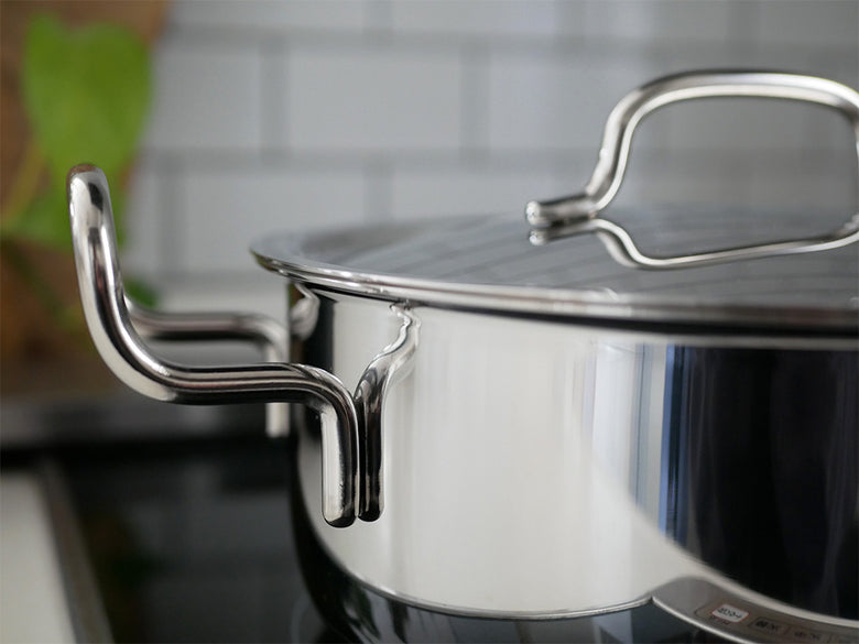 ステンレスとアルミニウム製の蓋付き鍋がキッチンのカウンターに置かれている