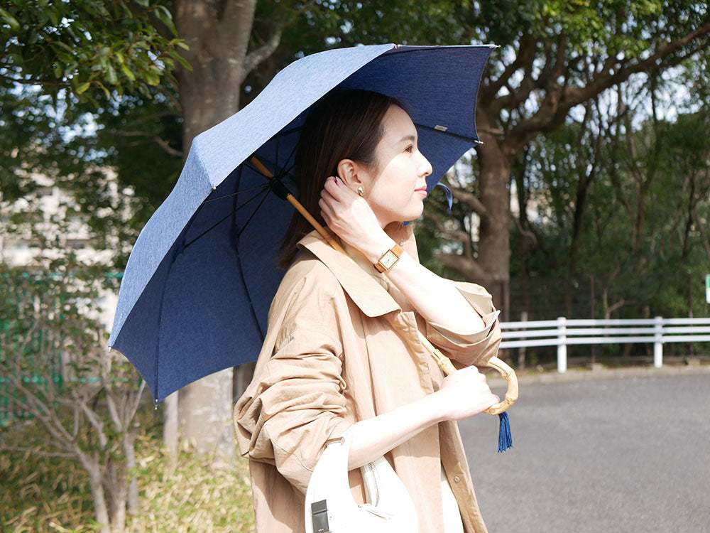 ビコーズのプレーンカラー傘を持つモデルがオーバーコートとハンドバッグを組み合わせたファッションを着用している写真