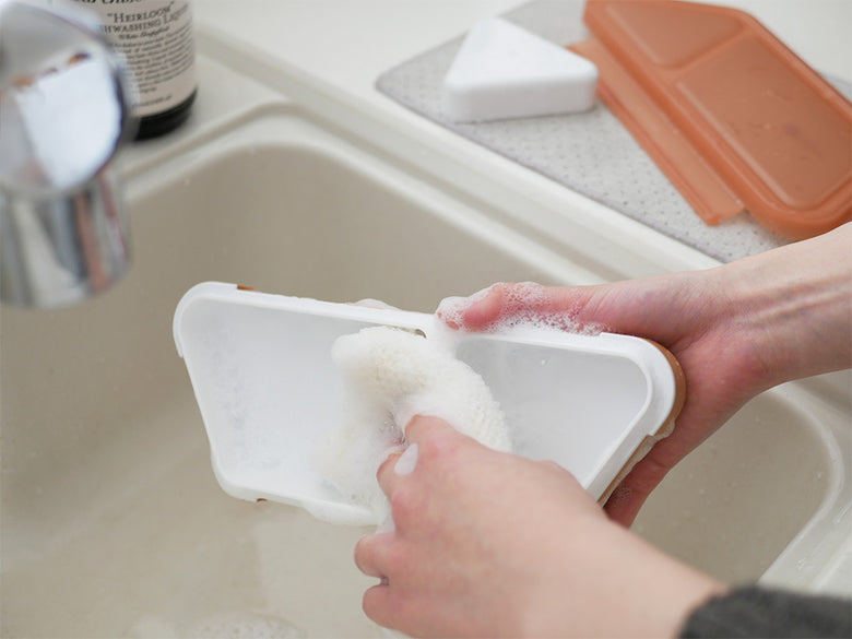 キッチンシンクにスポンジや家庭用洗剤、トレイなどの清掃用品が整然と配置された清潔な調理スペース