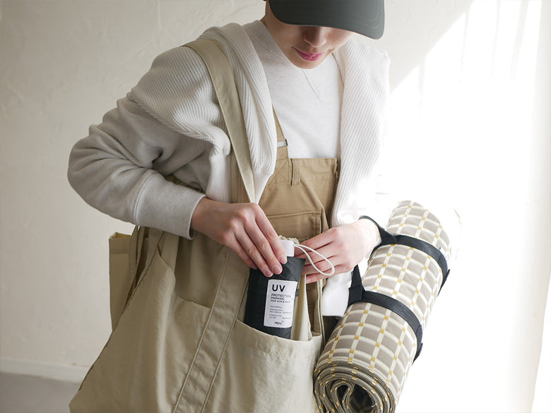 バッグやポケットが付いたエプロンを着用し、スマホサイズの折りたたみ傘を携帯している全体像の画像