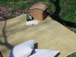 芝生に敷かれた黄色のパターン柄洗えるレジャーマットとアウトドア家具を使用したピクニック風景