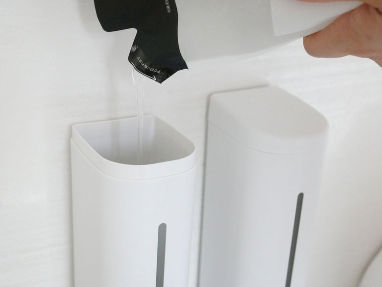 バスルームの壁に白色のシールフックディスペンサーが取り付けられ、蛇口やハンドドライヤー、ペーパータオルと共に整然と配置されている様子