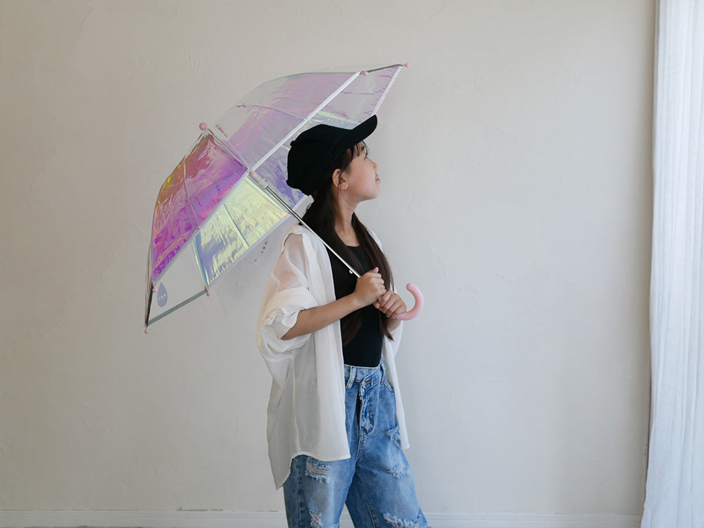 シャイニーなピンク色の子供用アンブレラを持ち、デニムとレギンスでスタイリングされたモデルのファッション写真