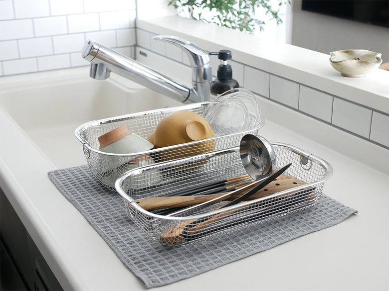 キッチンシンクに置かれたステンレス製のすっきり暮らす水切りかご。テーブルウェアや調理器具が整然と収納されています。