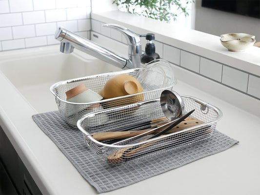 キッチンシンクに置かれたステンレス製のすっきり暮らす水切りかご。テーブルウェアや調理器具が整然と収納されています。