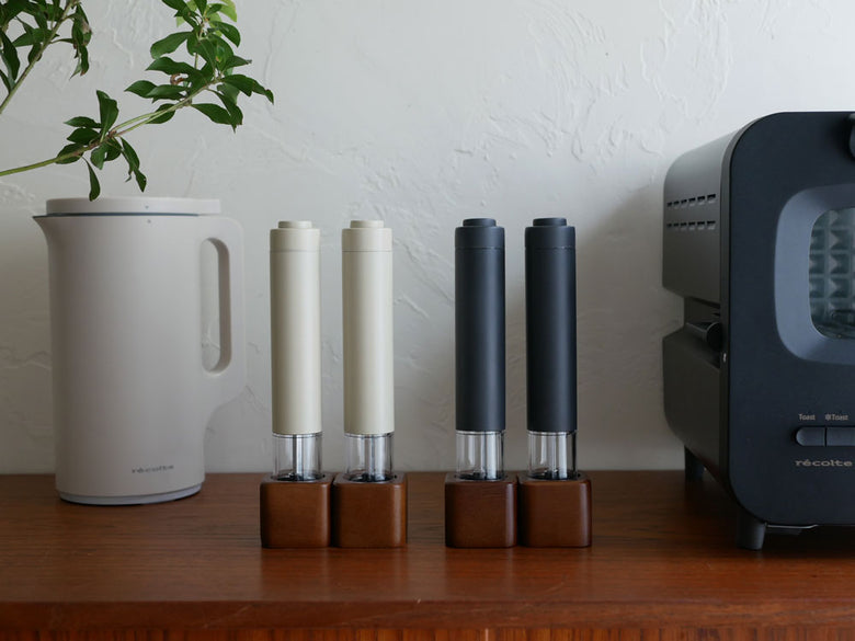 レコルトのアカシアスタンド付き電動ソルト＆ペッパーミル。クリームホワイトとグレーの円筒型本体と木製スタンドがセットされた家庭用電子機器の画像