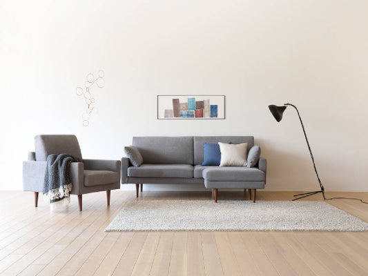 高野木工のLEOカウチソファが木製フローリングのリビングルームに配置され、アームレスト付きチェアとスタイリッシュなランプがアクセントとなっている様子