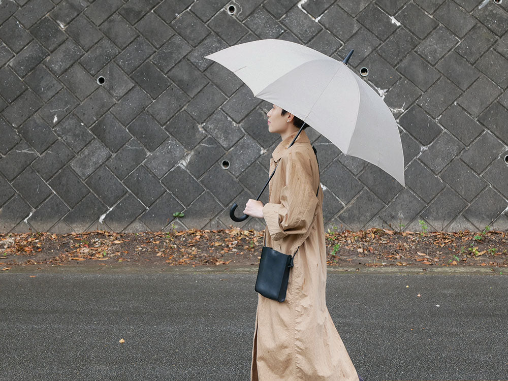 灰色のマーナ Shupattoアントブレラを持ち、オーバーコートを着て雨中を歩くファッショナブルな人物