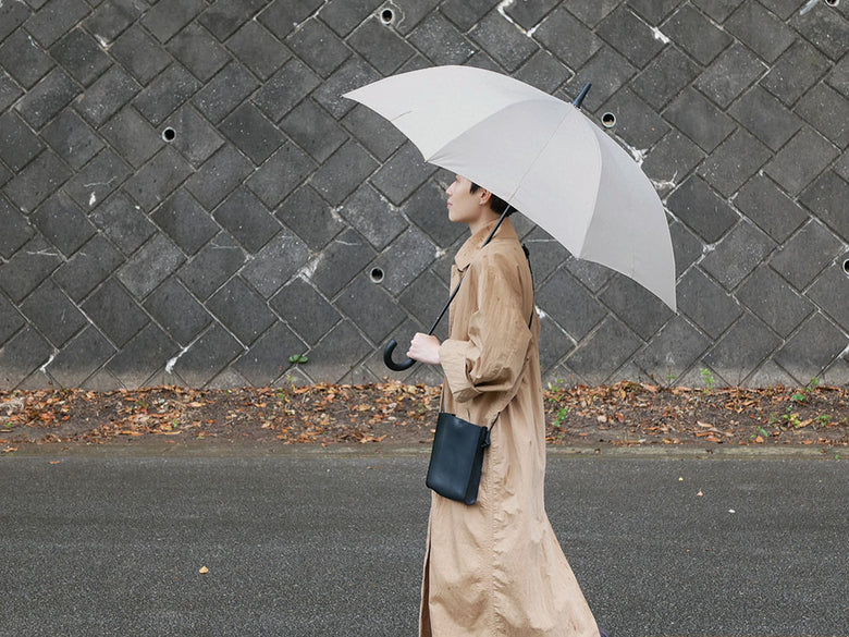 灰色のマーナ Shupattoアントブレラを持ち、オーバーコートを着て雨中を歩くファッショナブルな人物