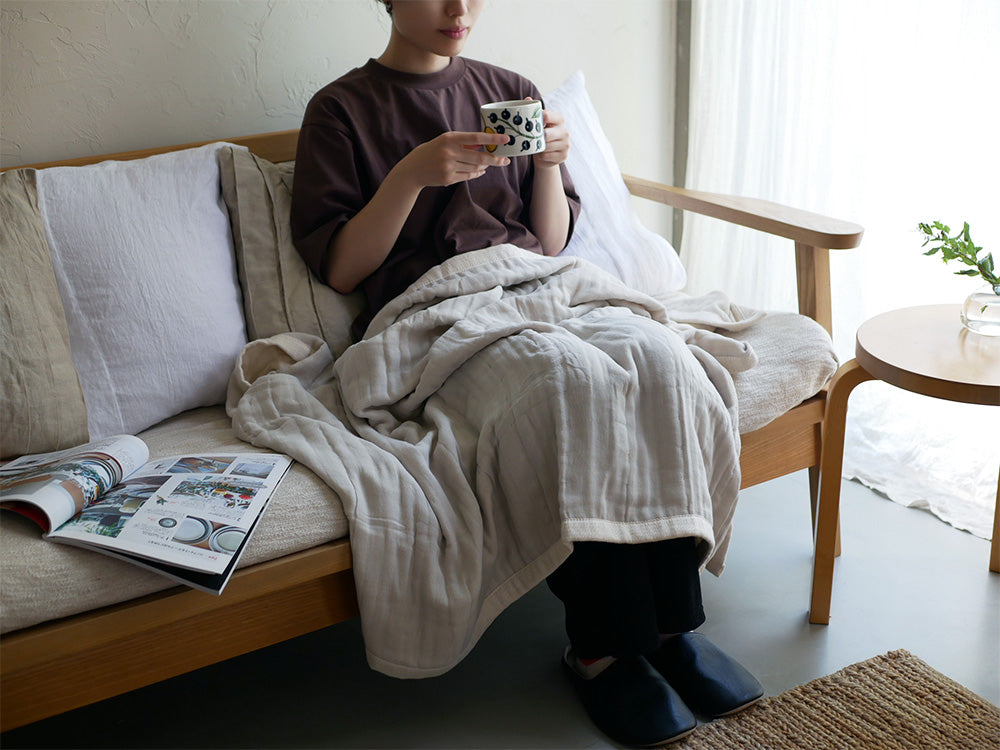 家具とクッションが配置された室内の床にシングルサイズのココマニとろサラ5重織ガーゼケットが敷かれている様子