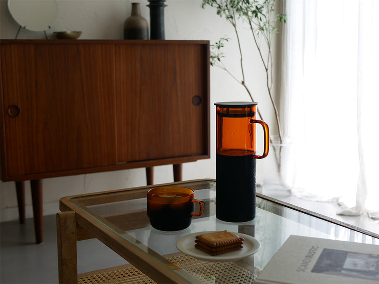 木目のテーブルに置かれたハリオの耐熱ガラスコールドブリューピッチャーとスタックマグ