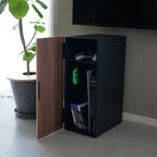 スチールと天然木を組み合わせたタワー型ゲーム機収納ラック。複数の棚に本やスピーカー、観葉植物が配置されたモダンな家具