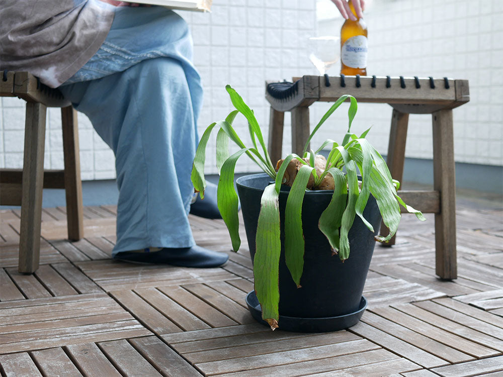 木製デッキの上にアマブロ ART STONE グレーのプラントポットが置かれ、周囲にアウトドア用テーブルや家具が配置されている様子