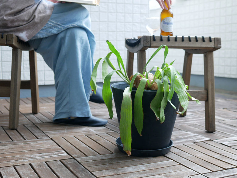 木製デッキの上にアマブロ ART STONE グレーのプラントポットが置かれ、周囲にアウトドア用テーブルや家具が配置されている様子