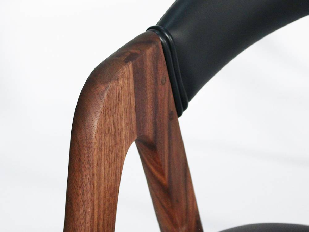 ブラウンのアデペシュ コバクホールドアームチェア。革張りと無垢材を使用し、三角デザインのアームレストが特徴