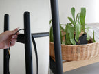 ラタンバスケット付き【NOWHERE LIKE HOME】のコートハンガーが室内に設置され、花鉢と室内植物が周囲に配置されている