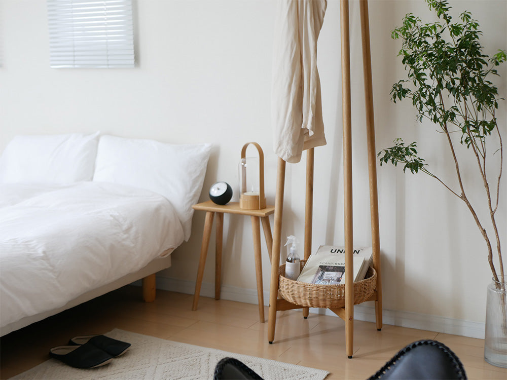 オーク無垢材とラタンバスケットを備えたコートハンガーが、木製の床と家具と共に整った室内に配置されている様子