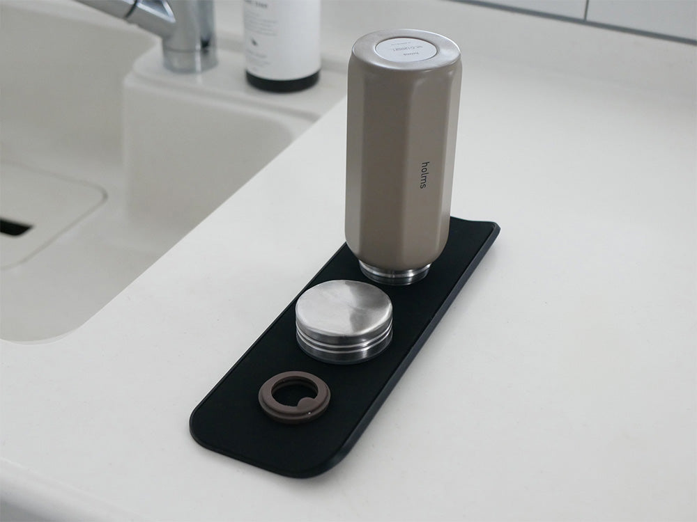 シンク上に置かれた【stta/スッタ】超速乾・超吸水２way水切りマット＆クロス。銀色の蛇口やソープディスペンサー、家の植物が周囲に配置され、デザイン性の高いキッチン用品が映し出されています。