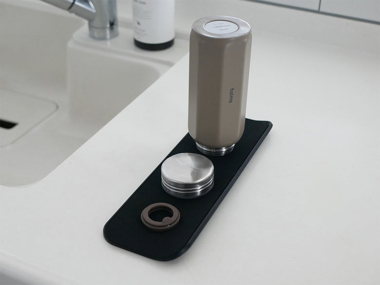 シンク上に置かれた【stta/スッタ】超速乾・超吸水２way水切りマット＆クロス。銀色の蛇口やソープディスペンサー、家の植物が周囲に配置され、デザイン性の高いキッチン用品が映し出されています。