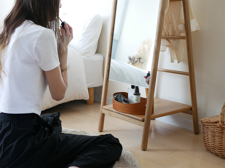 オーク材の収納スタンドミラーと花鉢、観葉植物、ランプ、スツール、花瓶が配置された居室のインテリア