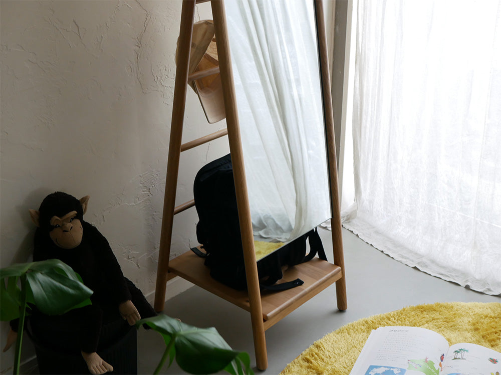 オーク材の収納機能付きスタンドミラー『SCALA』が、木製フローリングとカーテン、室内植物と共に配置されたリビングルームに設置されている様子