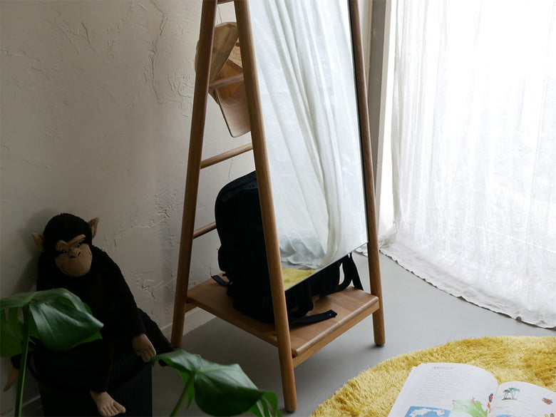 オーク材の収納機能付きスタンドミラー『SCALA』が、木製フローリングとカーテン、室内植物と共に配置されたリビングルームに設置されている様子